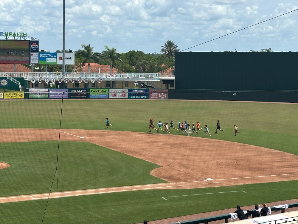 Children run across the outfield of a professional baseball stadium on a cloudy day